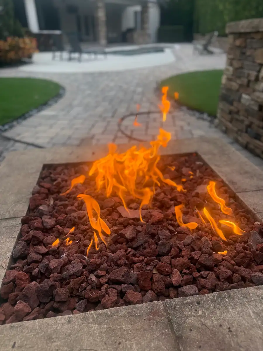 A lit fire pit of red lava rock on a paver patio