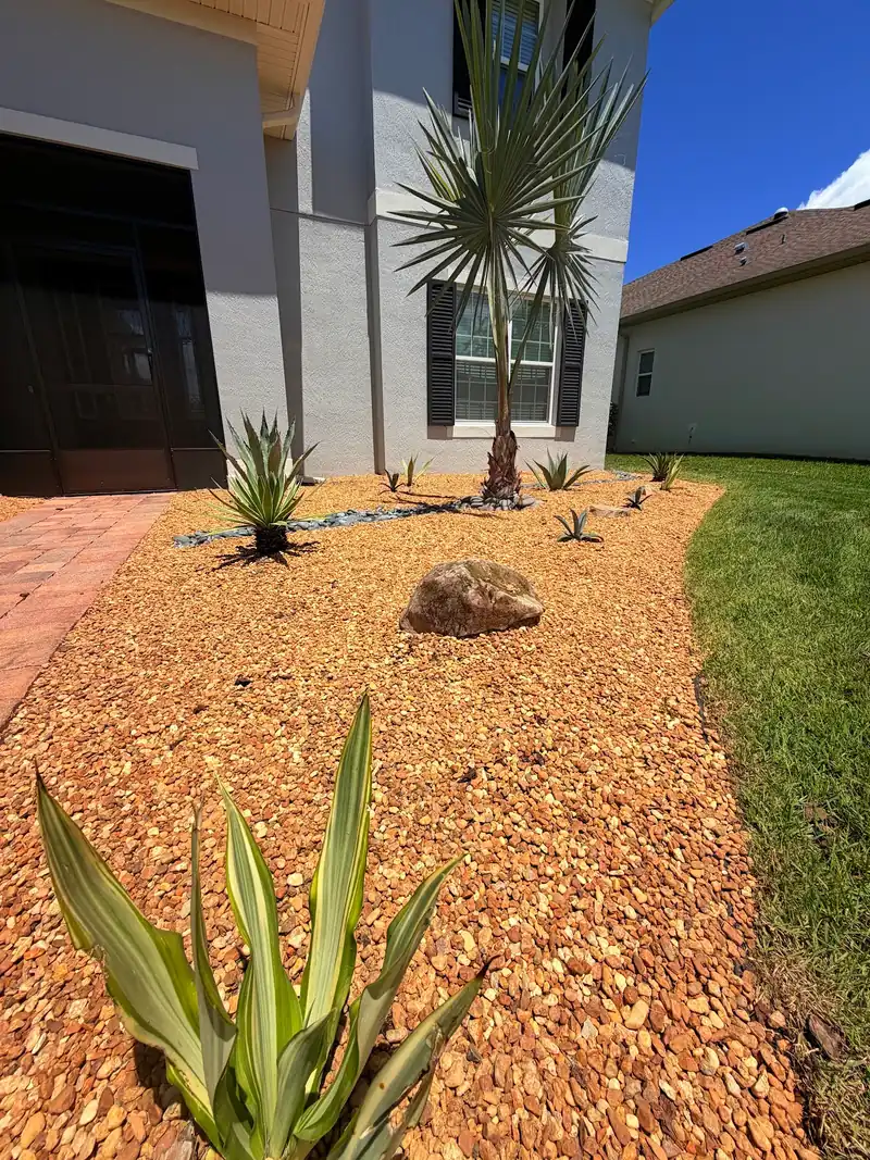 A finished front bed of river rock, agaves and a palm